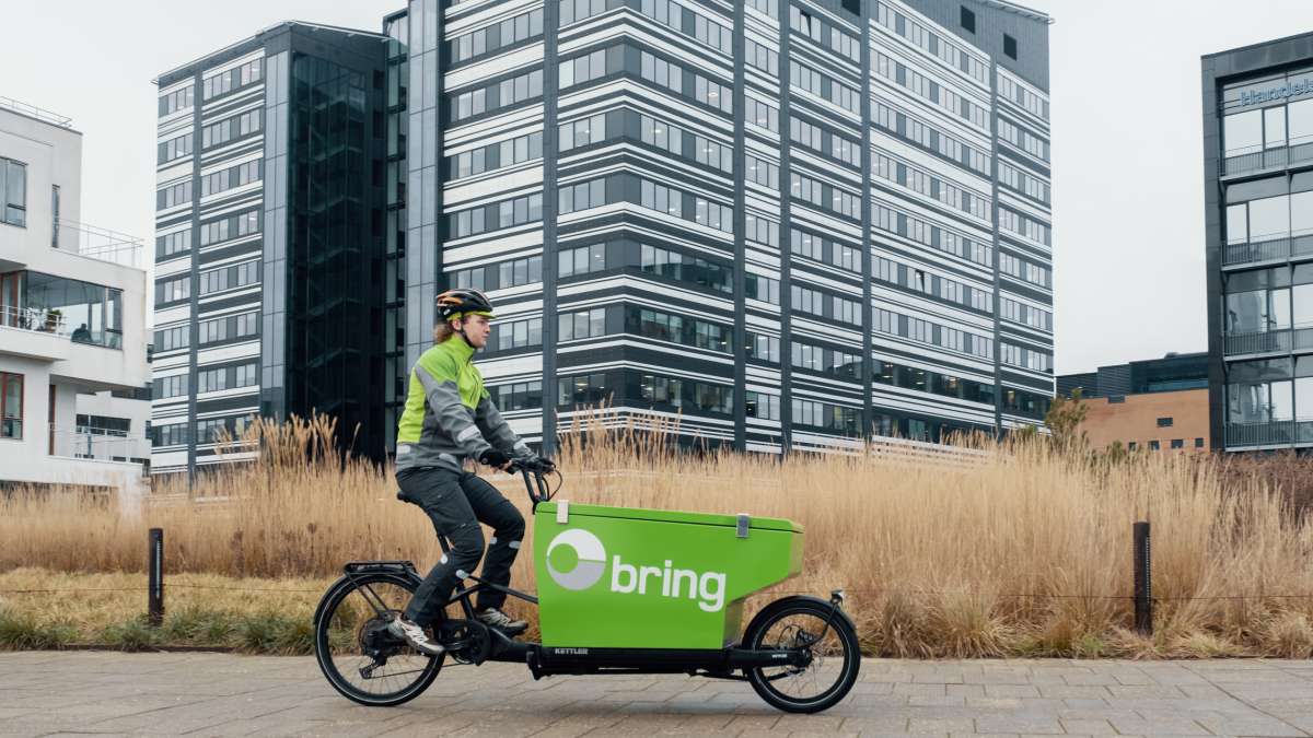 Bringbud på grønn elsykkel transporterer pakker i et boligområde.