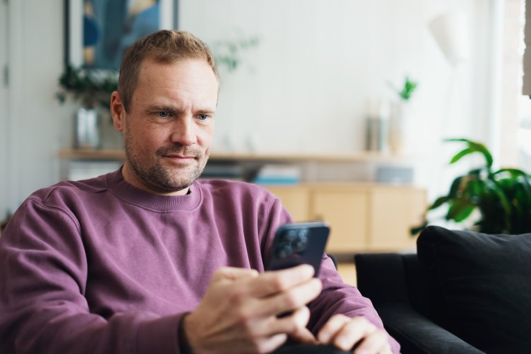 En mann sitter og ser på en mobiltelefon som han holder i hånden