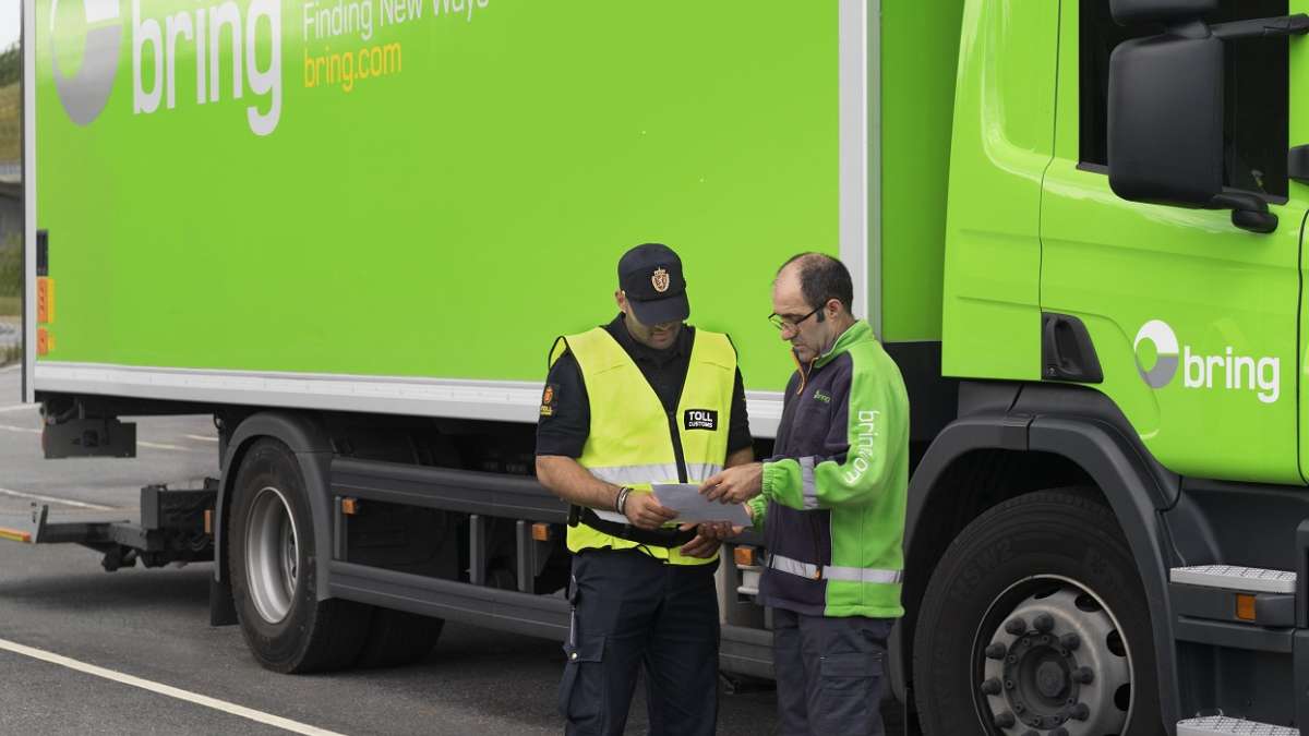 Tollansatt snakker med brinsjåfør over dokumenter ved lastebil fra Bring.